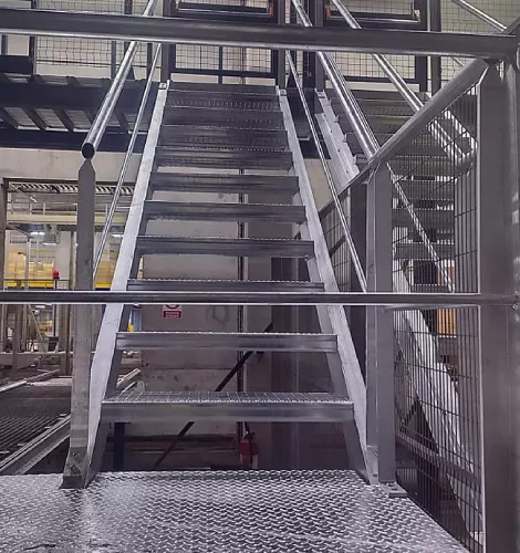 Escalier métallique dans un entrepôt avec garde-corps et plateforme d’accès