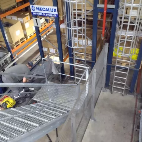 Travailleurs installant un escalier métallique dans un entrepôt avec structures en acier