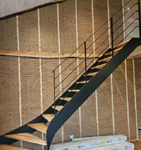Escalier avec rambarde métallique noire et mur en briques apparentes